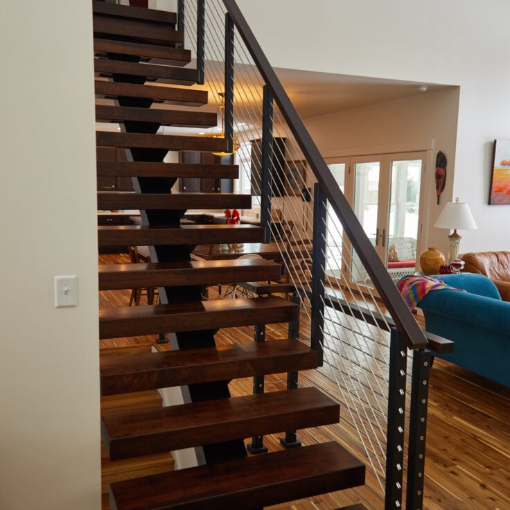 Floating stair system featuring stained hard maple treads & handrail, and rod railing, seen from the front.