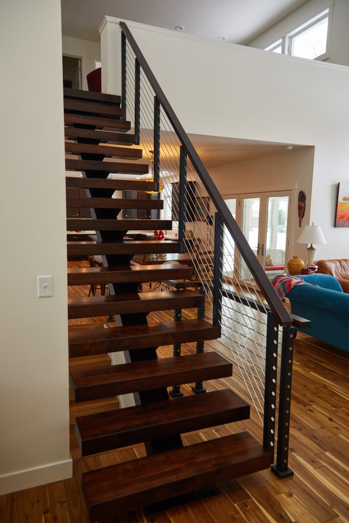 Floating stair system featuring stained hard maple treads & handrail, and rod railing, seen from the front.