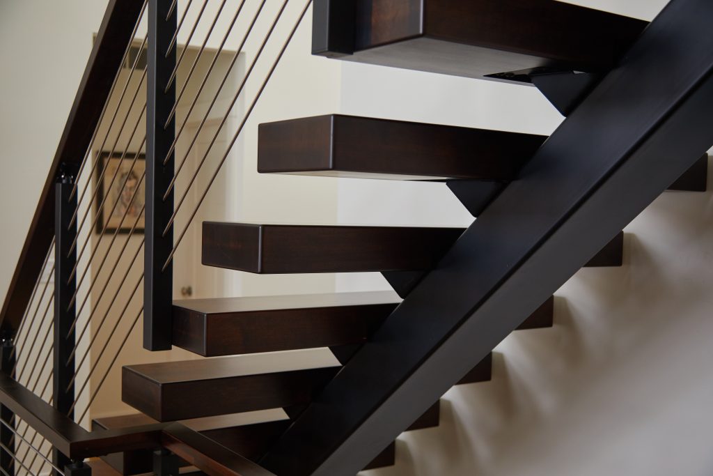 Close up of floating stair stringer, tread-side mounted rod railing posts, and stained hard maple treads.