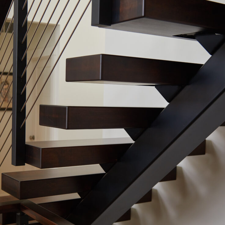 Close up of floating stair stringer, tread-side mounted rod railing posts, and stained hard maple treads.