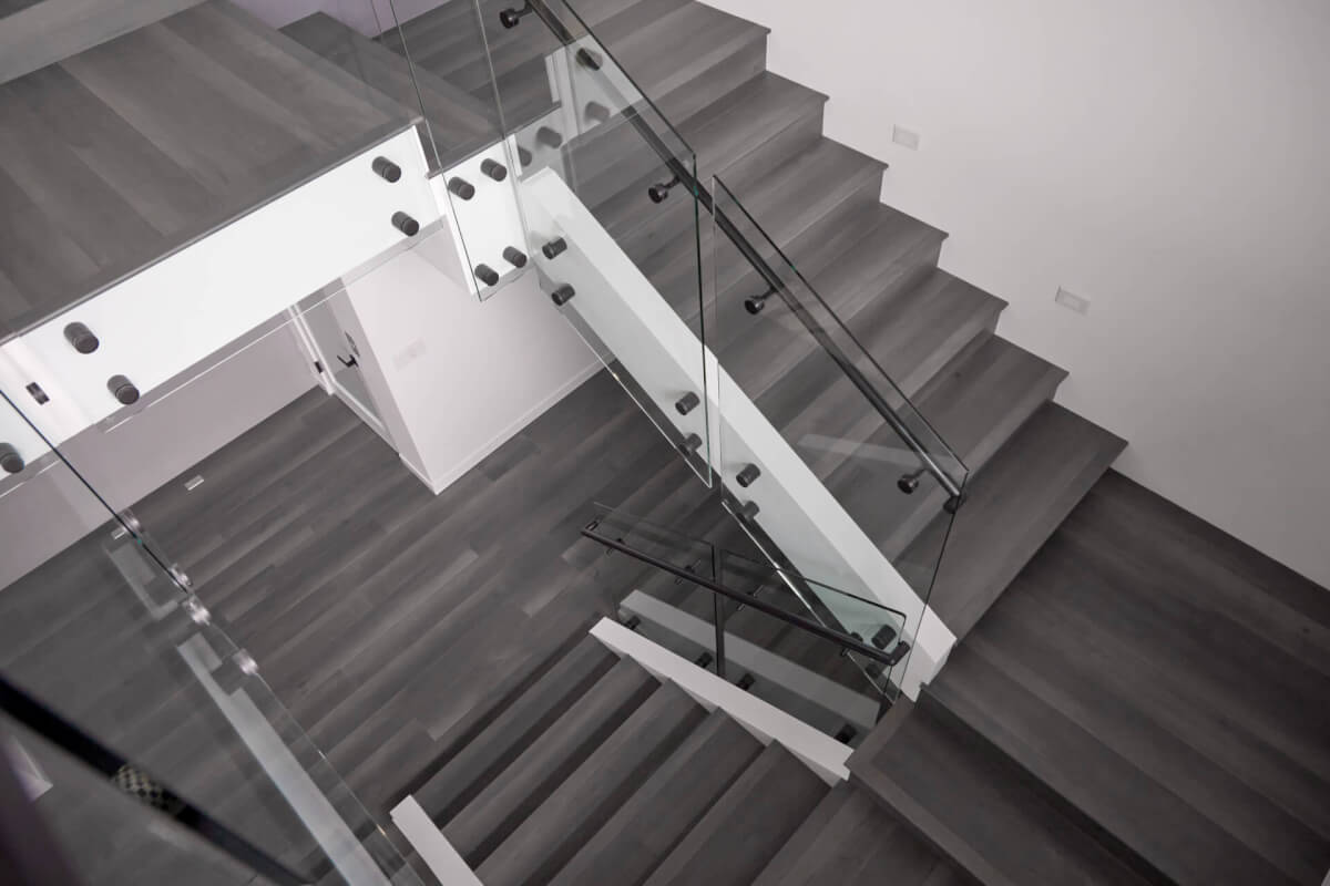 This house has dark flooring with clear stair railings. The walls are white, and there is black hardware on the railings. 