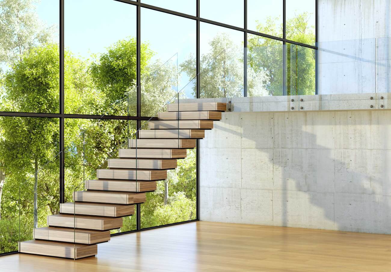 This large, open-concept room has a floating staircase with light wood-colored steps and a clear railing. The whole wall next to the staircase is windows, and the second floor has a clear railing as well. 