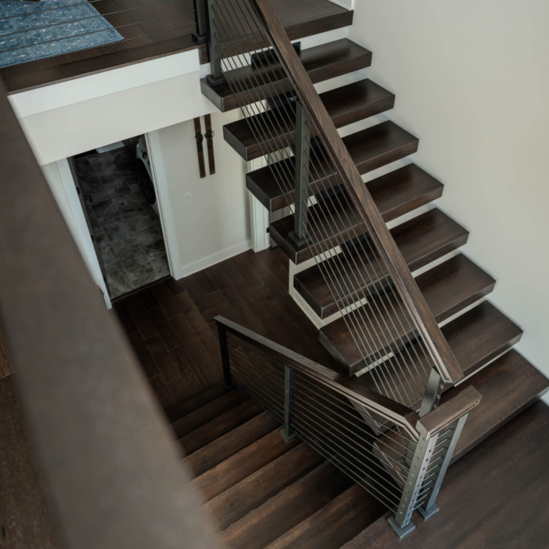 A photo looking down at floating stairs with Viewrail Signature Cable railing with dark wood handrail and onyx rod infill.