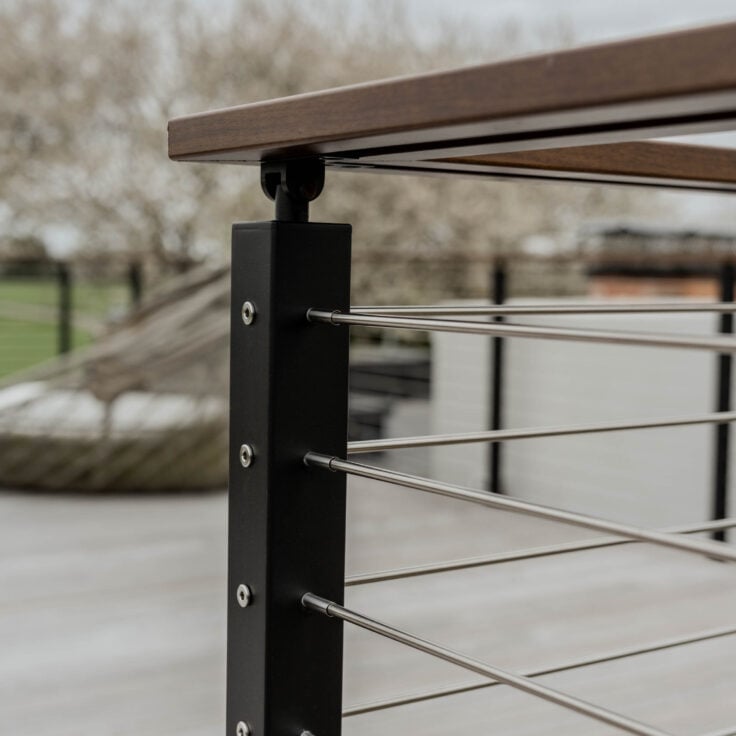 A closeup shot of the corner of a Signature cable railing with black metal posts, rod infill, and a wood handrail