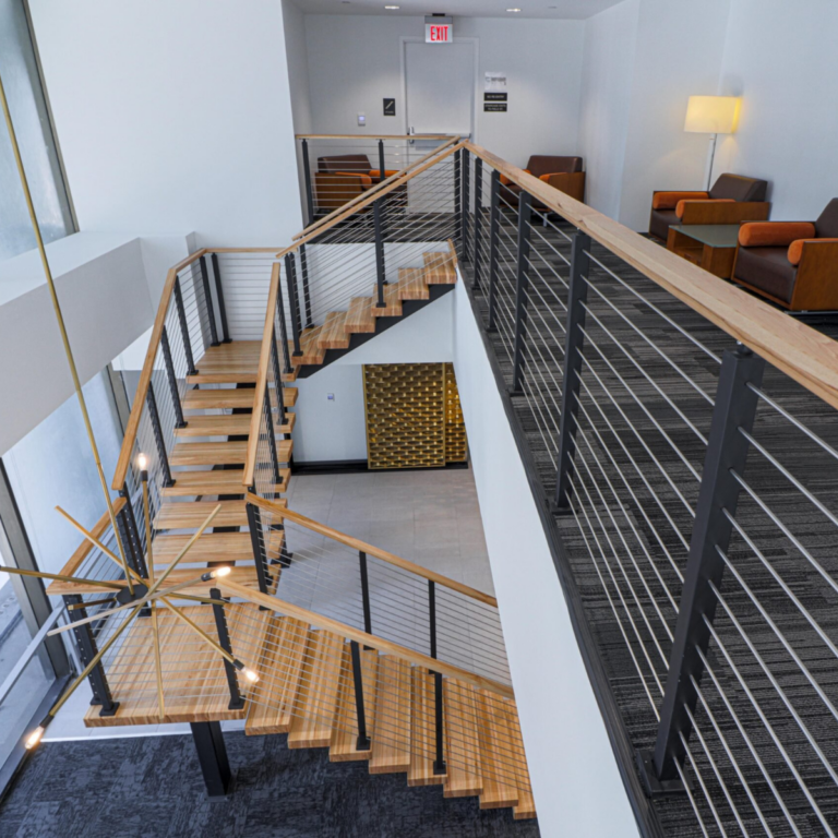 Viewrail Signature Cable Railing with wooden handrail and steel rod infill goes along a balcony and down a u-shaped floating staircase